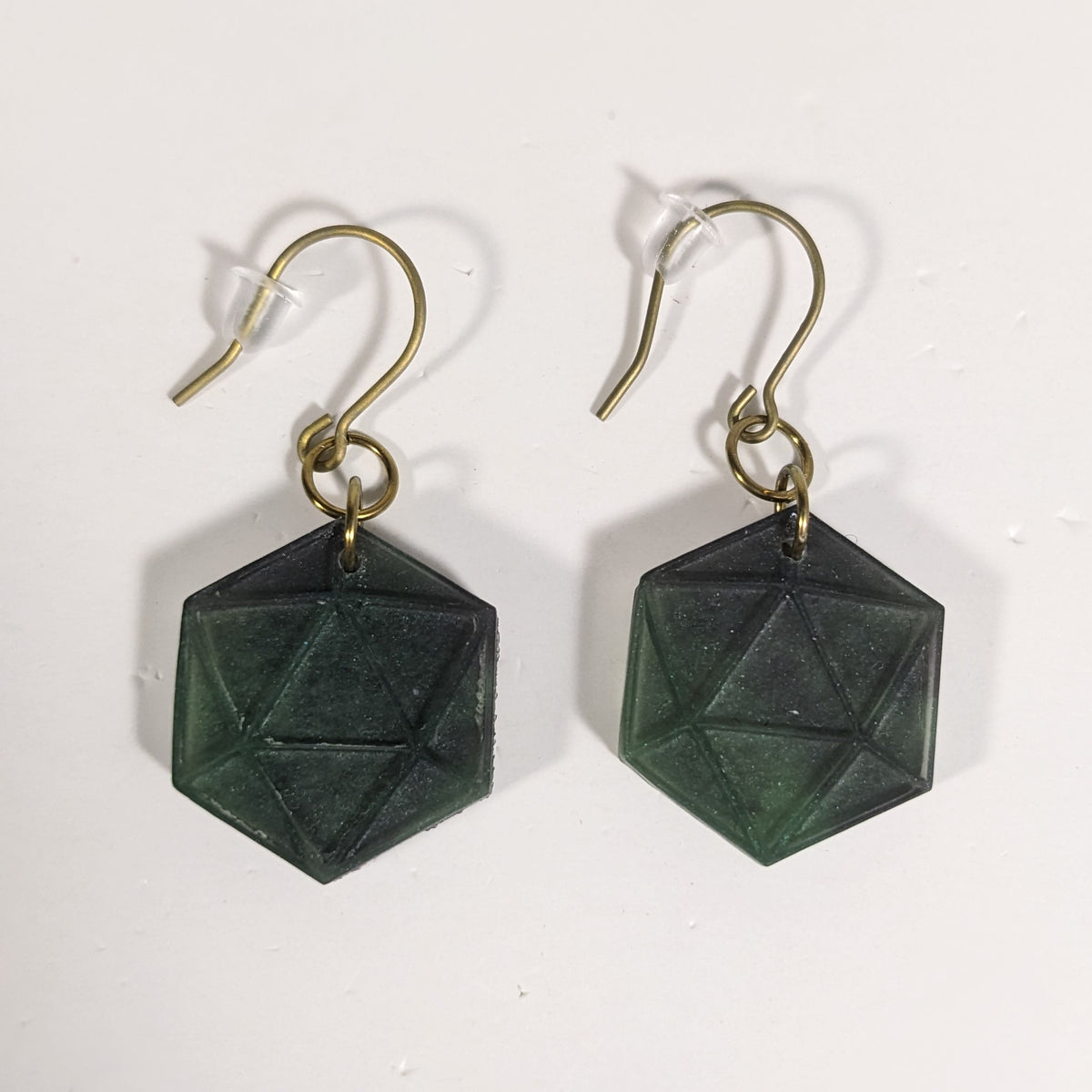 A pair of dark green and black dangly, flat d20 earrings with gold color titanium and niobium hardware and bell shaped rubber backs on a white background.