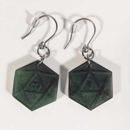 A pair of black and dark green dangly, flat d20 earrings with silver color titanium and niobium hardware and bell shaped rubber backs on a white background. The earring on the left has a 20 on it and the earring on the right has a 1 on it, both in a sci-fi style font.