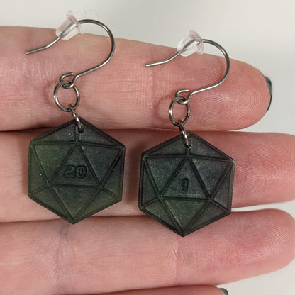 A pair of black and dark green dangly, flat d20 earrings with silver color titanium and niobium hardware with bell shaped rubber backs held on on a hand on a white background. The earring on the left has a 20 on it and the earring on the right has a 1 on it, both in a sci-fi style font.