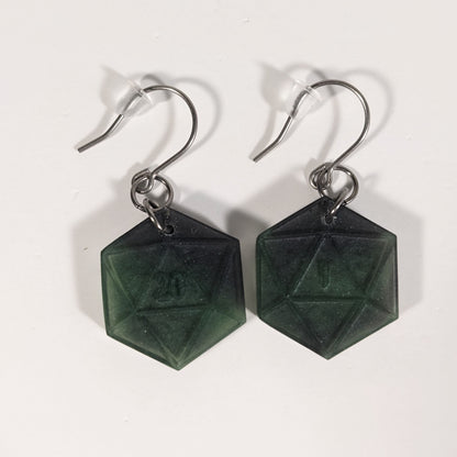 A pair of black and dark green dangly, flat d20 earrings with silver color titanium and niobium hardware and bell shaped rubber backs on a white background. The earring on the left has a 20 on it and the earring on the right has a 1 on it, both in a fantasy style font.