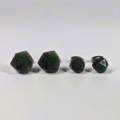 Two pairs of handmade d20 earrings that are dark green and black with red numbers on a white background sit in a line with the larger pair on the left and the smaller pair on the right. The earrings on the left of each pair centers the 20 face and the earrings on the right of each pair centers the 1 face.