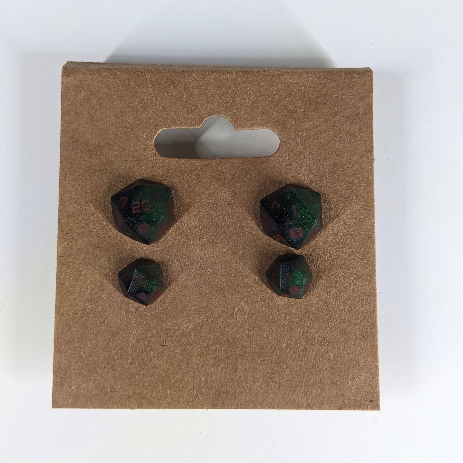Two pairs of handmade d20 earrings that are dark green and black with red numbers on a kraft brown earring card. The earrings on the left of each pair centers the 20 face and the earrings on the right of each pair centers the 1 face.