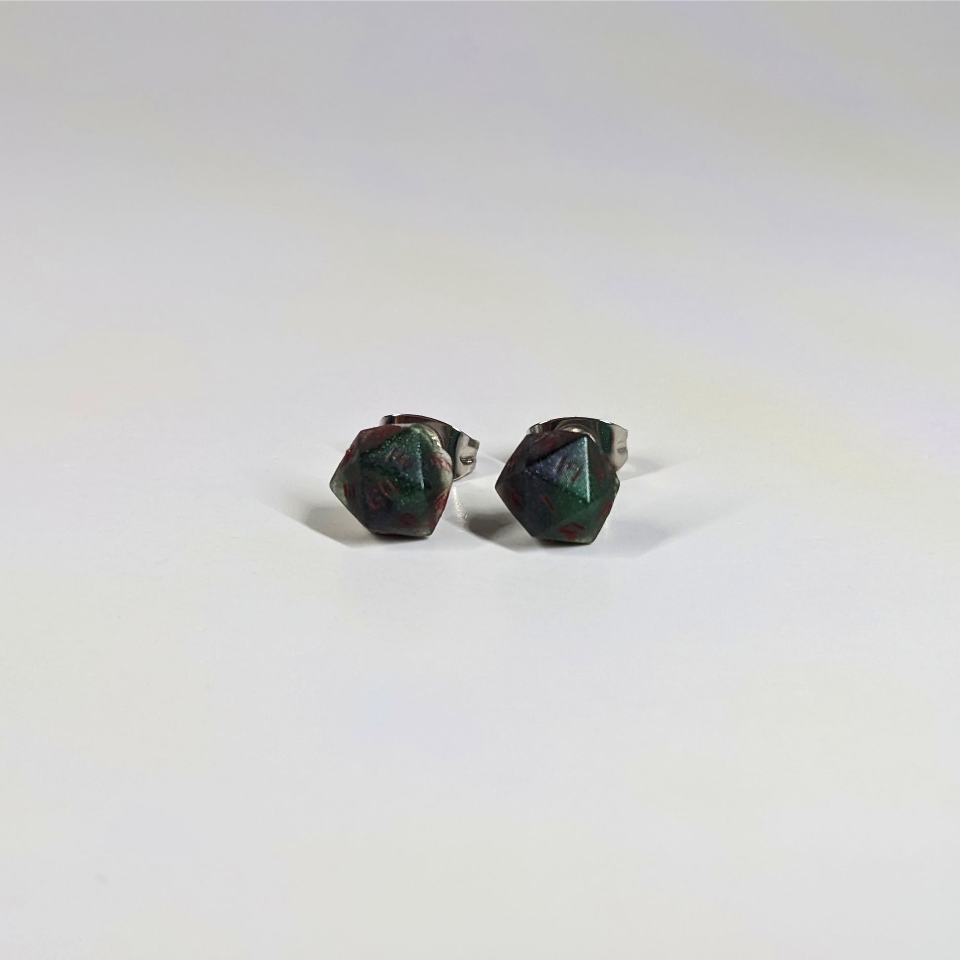 A single pair of the smaller size handmade d20 earrings that are dark green and black with red numbers on a white background. The earring on the left centers the 20 face and the earring on the right centers the 1 face.