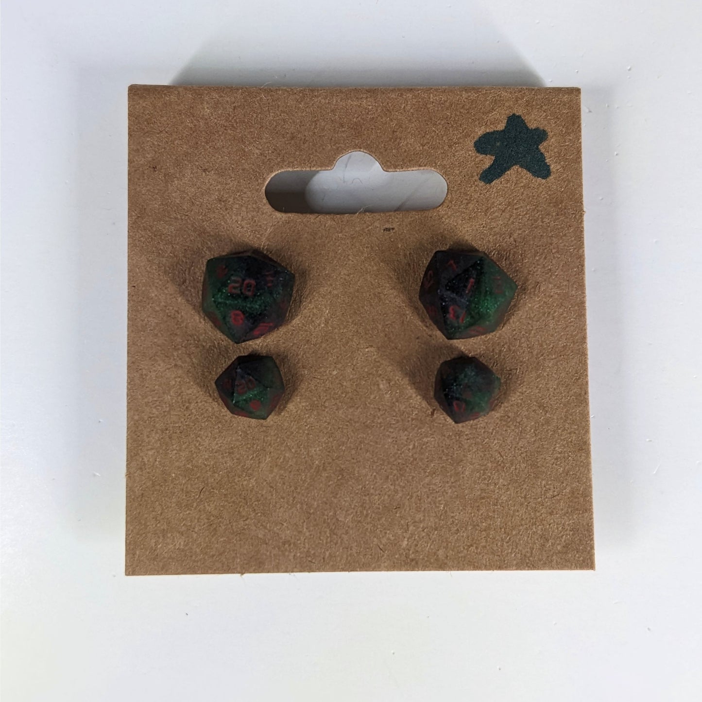 Two pairs of handmade d20 earrings with sterling silver hardware that are dark green and black with red numbers on a kraft brown earring card with a star in the top right corner. The earrings on the left of each pair centers the 20 face and the earrings on the right of each pair centers the 1 face.