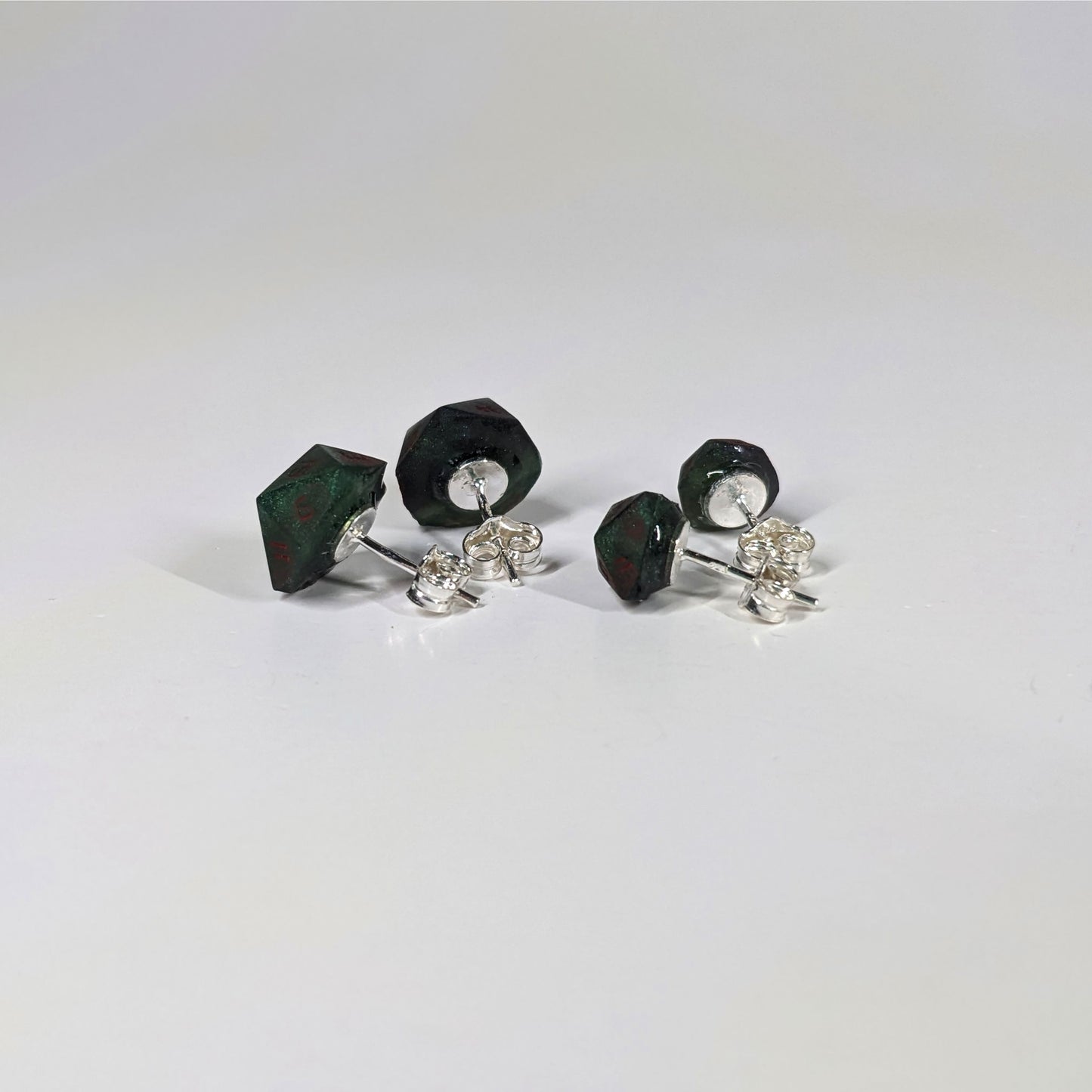 Two pairs of handmade d20 earrings that are dark green and black with red numbers turned to show the sterling silver hardware and butterfly backs.