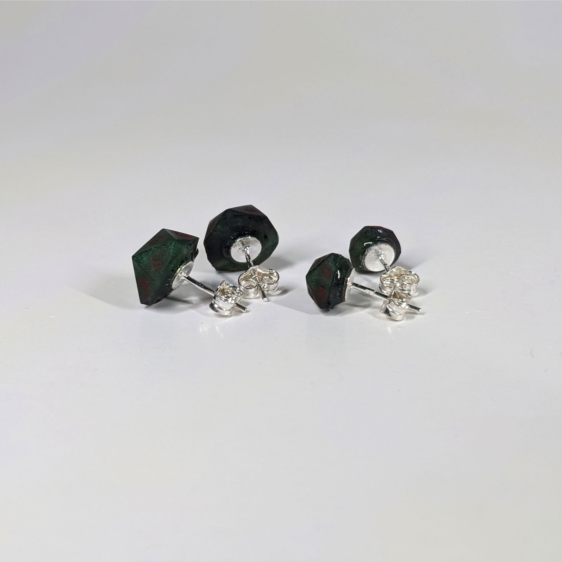Two pairs of handmade d20 earrings that are dark green and black with red numbers turned to show the sterling silver hardware and butterfly backs.