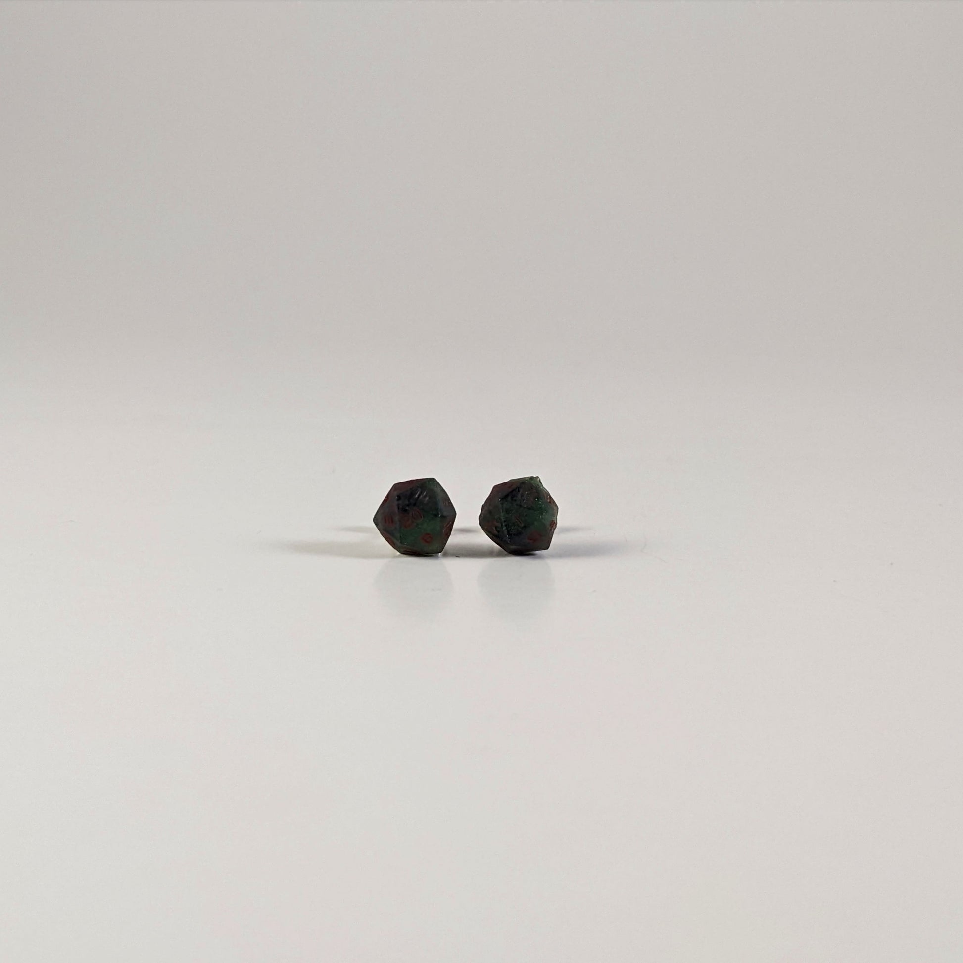 A single pair of the smaller size handmade d20 earrings with sterling silver hardware that are dark green and black with red numbers on a white background. The earring on the left centers the 20 face and the earring on the right centers the 1 face.