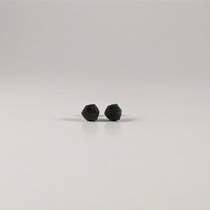 A single pair of the smaller size handmade d20 earrings with sterling silver hardware that are dark green and black with red numbers on a white background. The earring on the left centers the 20 face and the earring on the right centers the 1 face.