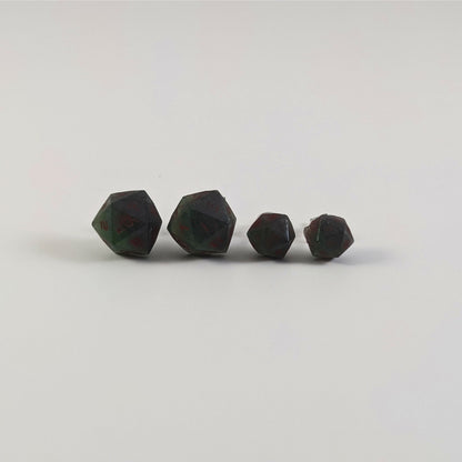 Two pairs of handmade d20 earrings with titanium hardware that are dark green and black with deep red numbers on a white background sit in a line with the larger pair on the left and the smaller pair on the right. The earrings on the left of each pair centers the 20 face and the earrings on the right of each pair centers the 1 face.