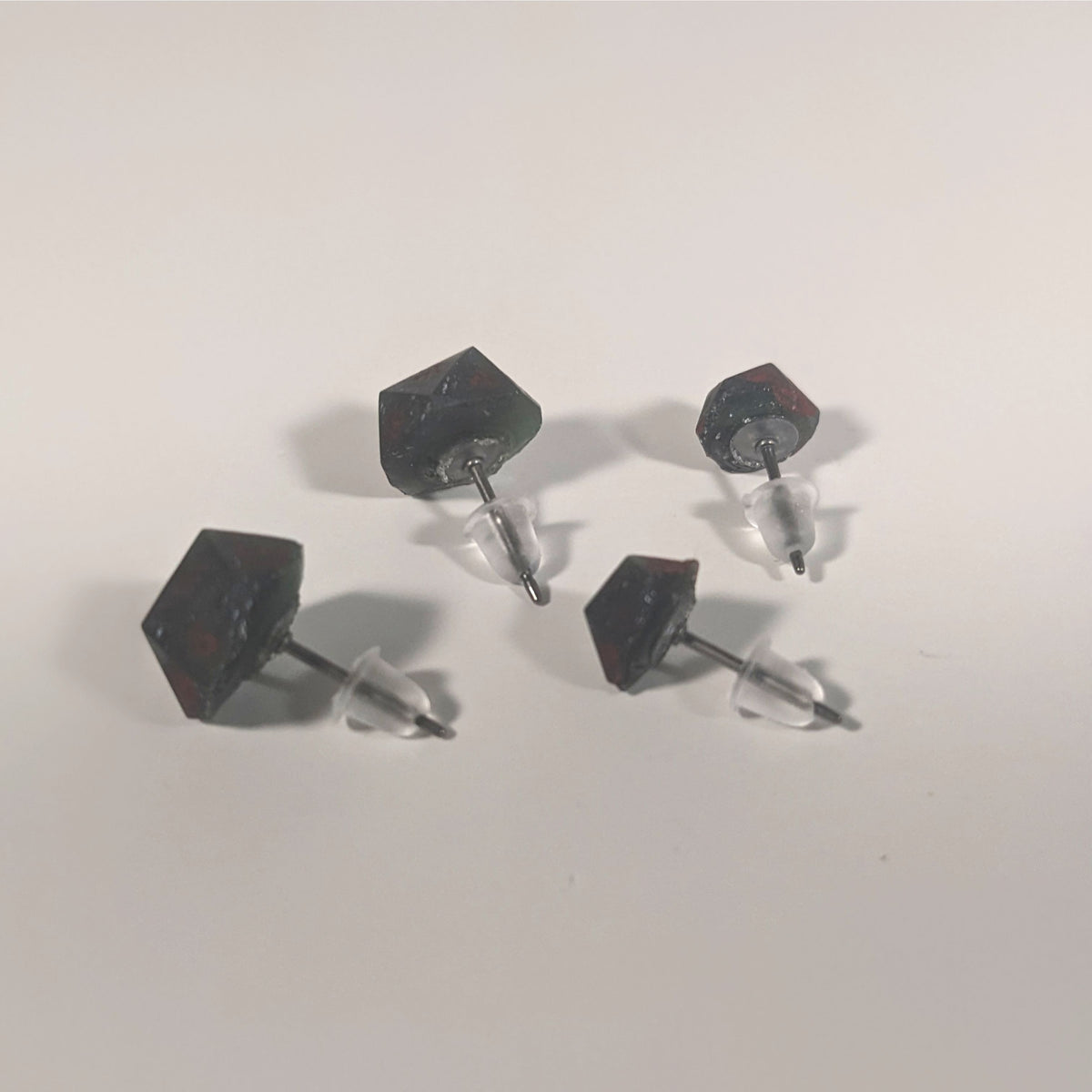 Two pairs of handmade d20 earrings that are dark green and black with deep red numbers turned to show the titanium hardware and bell shaped rubber backs.