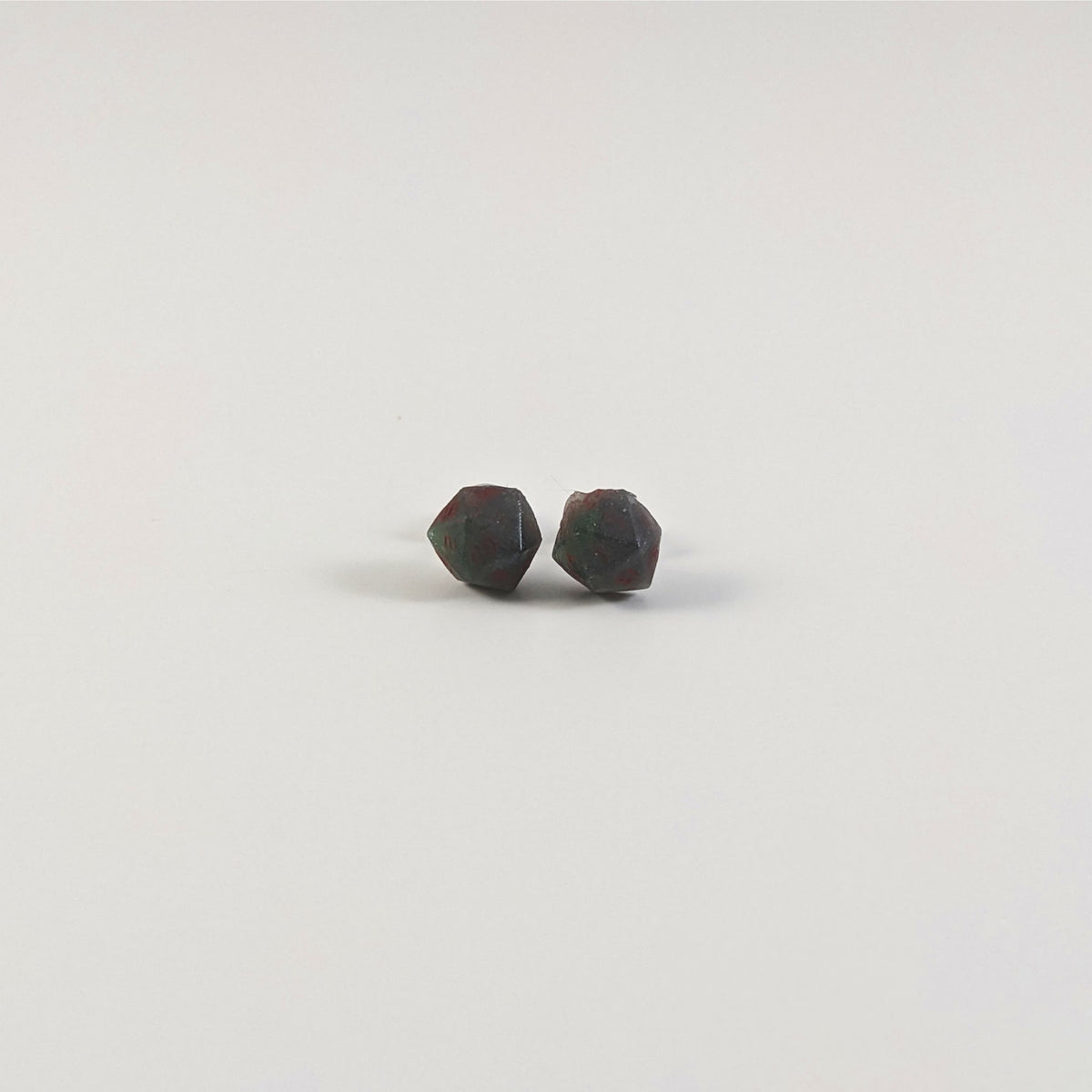 A single pair of the smaller size handmade d20 earrings with titanium hardware that are dark green and black with deep red numbers on a white background. The earring on the left centers the 20 face and the earring on the right centers the 1 face.