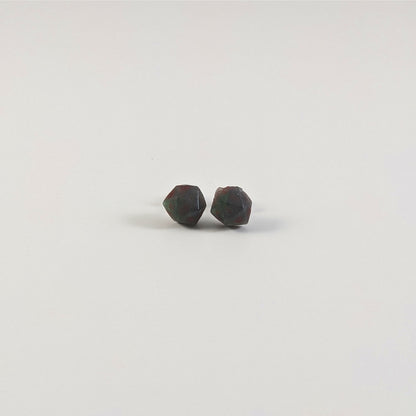 A single pair of the smaller size handmade d20 earrings with titanium hardware that are dark green and black with deep red numbers on a white background. The earring on the left centers the 20 face and the earring on the right centers the 1 face.