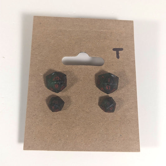 Two pairs of handmade d20 earrings with titanium hardware that are dark green and black with deep red numbers on a kraft brown earring card with a T in the top right corner. The earrings on the left of each pair centers the 20 face and the earrings on the right of each pair centers the 1 face.