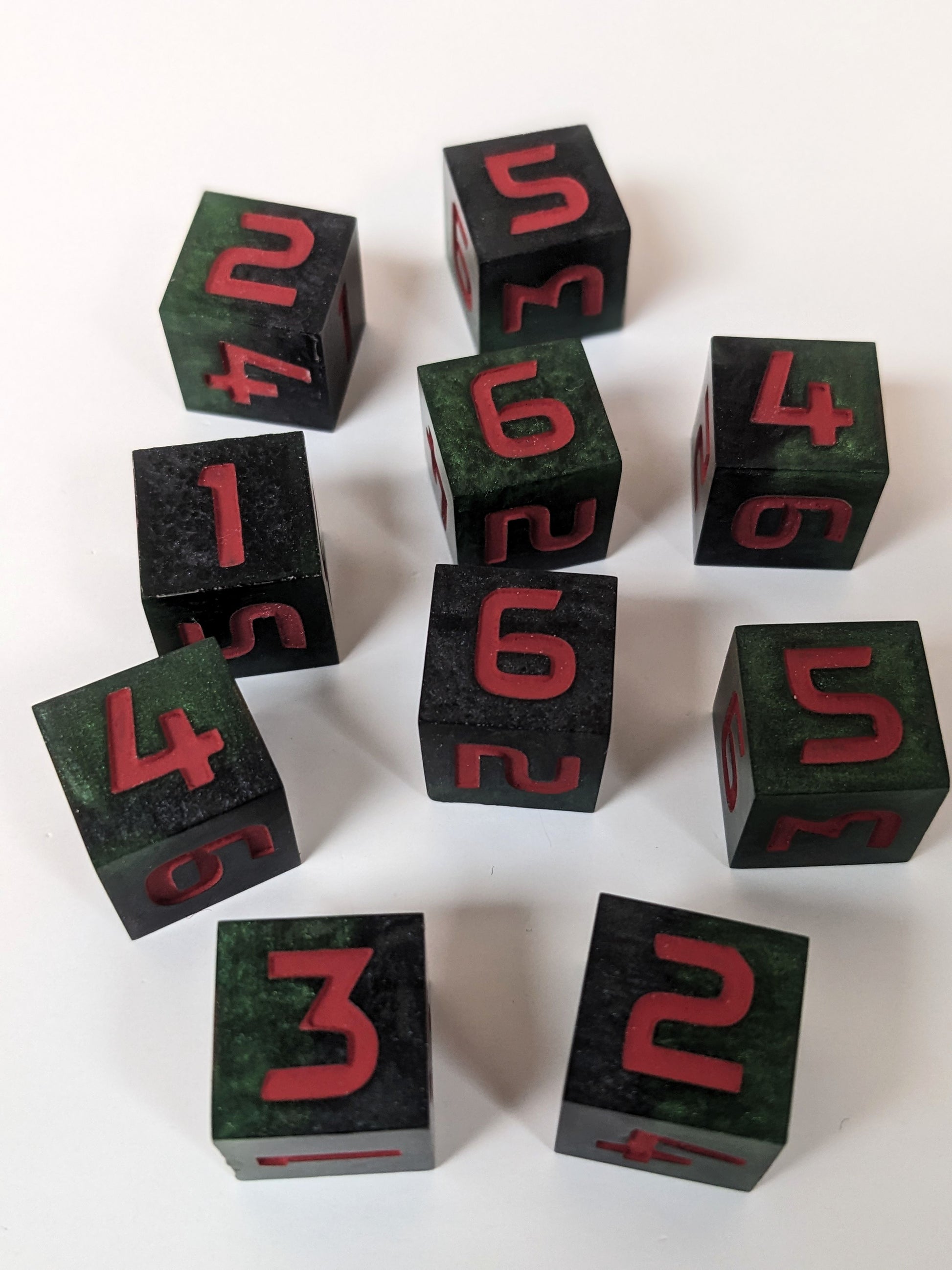 Ten standard six sided dice sit on a white background. The dice are black and dark green with red numbers.