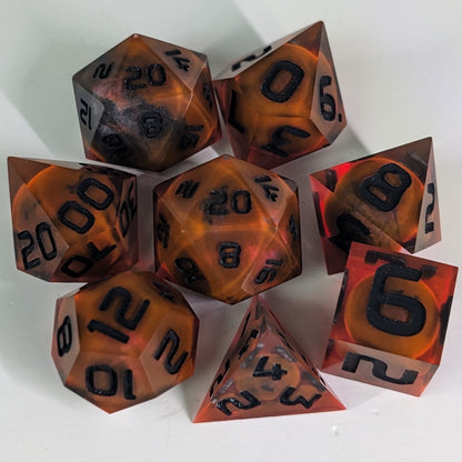 A complete set of 8 handmade artisan dice that are a glowy red-orange with dark spherical inserts and black numbers. The DnD dice set is arranged in a circle and features 2 D20s, one of which is in the center surrounded by the other 7 dice.