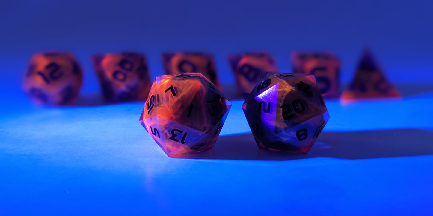 A straight on photo of a standard set of DnD dice that are a glowy red-orange that is extra bright reacting to a UV light with dark spherical inserts and black numbers focusing on 2 d20s in the center. The d20 on the left has the 1 face centered and the d20 on the right has the 20 face centered. The other 6 dice are lined up in the background but are out of focus, while the d20s are in sharp focus. The lighting is tinged blue from the UV light.