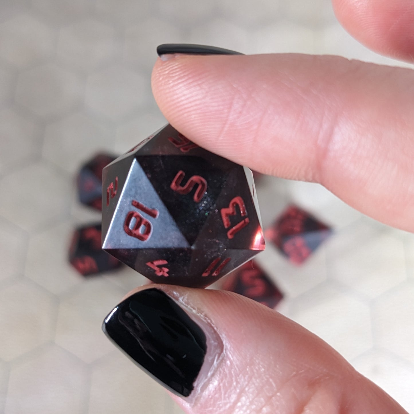 A d20 that has a dark spherical insert with red swirls in the shell and red numbers is held up to the camera to show off the red-orange swirls around the dark, spherical insert and otherwise clear shell. The 18 and 5 faces are most angled toward the camera.