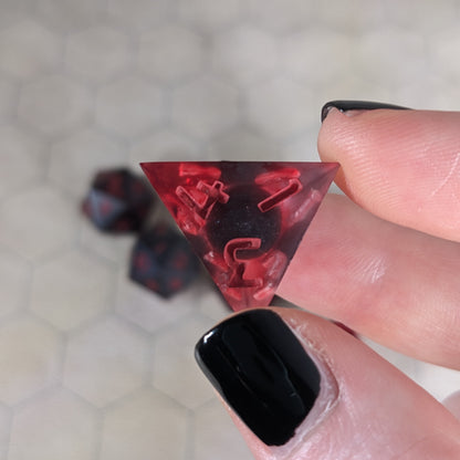 A d4 that has a dark spherical insert with red swirls in the shell and red numbers is held up to the camera to show off the red-orange swirls around the dark, spherical insert and otherwise clear shell. The face with 4, 3, and 1 in the corners is most angled toward the camera.