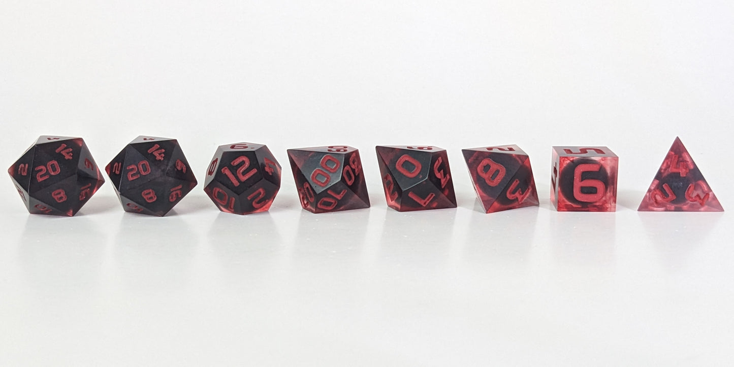 A straight on photo of a complete set of polyhedral dice that have dark, spherical inserts with swirls of red in the shell and red numbers arranged in a straight line. They are lined up with the 2 d20s on the left going down to the d4 on the right side. The highest value number of each die is facing forward.