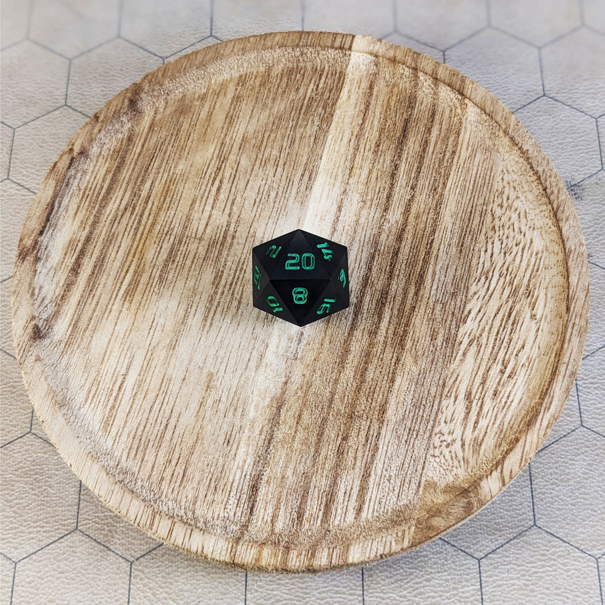 A standard d20 with black swirls and green numbers sits in the center of a wooden circle on a beige hex map.