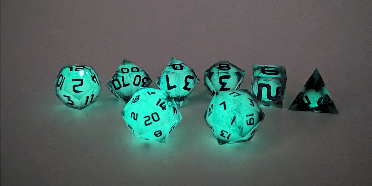 A straight on photo of a standard set of DnD dice that have black swirls showing through glow-in-the-dark green spherical insert and purple numbers focusing on 2 d20s in the center. The d20 on the left has the 20 face centered and the d20 on the right has the 1 face centered. The other 6 dice are lined up in the background.