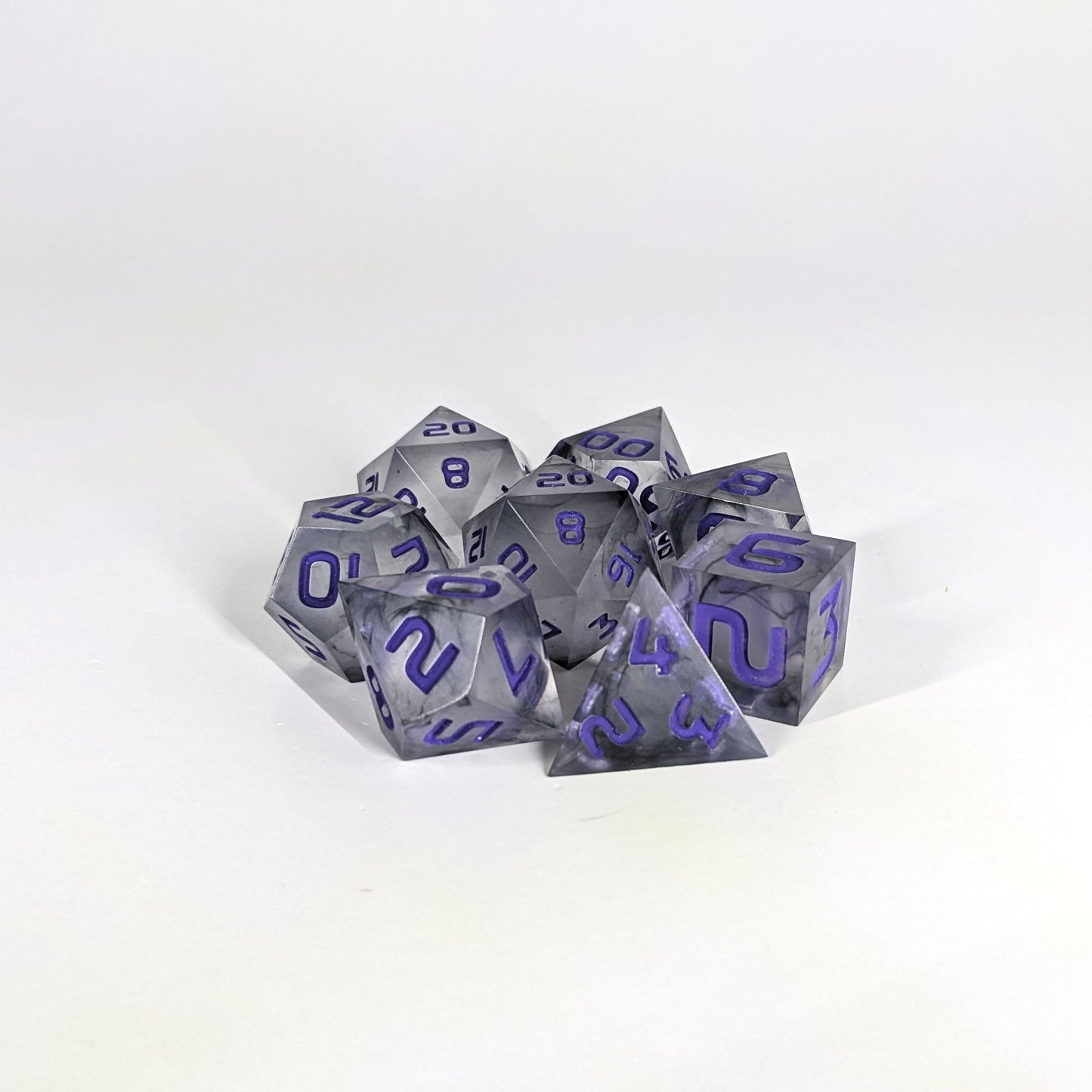 A complete set of 8 handmade artisan dice that have black swirls around a cloudy spherical insert with purple numbers. The DnD dice set is arranged in a circle and features 2 D20s, one of which is in the center surrounded by the other 7 dice.