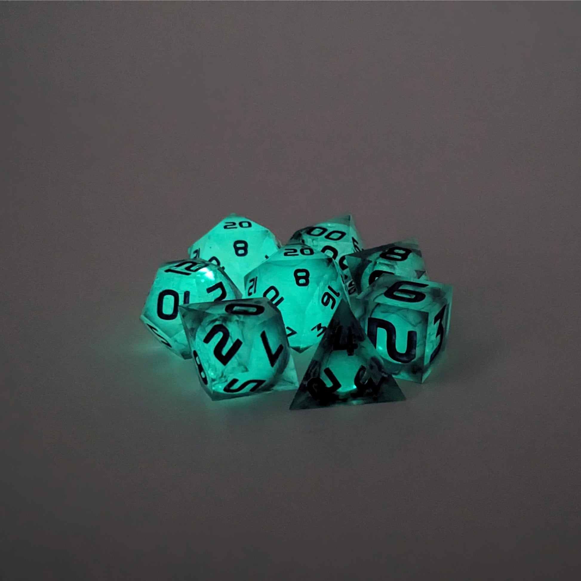 A complete set of 8 polyhedral dice that with spherical inserts glowing green, black swirls and purple numbers, showing the glow-in-the-dark feature of this dice set. The DnD dice set is arranged in a circle and features 2 D20s, one of which is in the center surrounded by the other 7 dice.