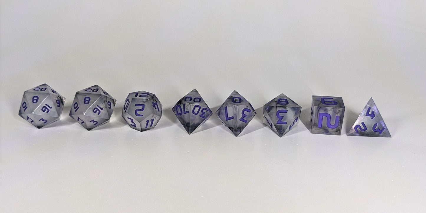 A straight on photo of a complete set of polyhedral dice that have black swirls around a cloudy, spherical insert and purple numbers arranged in a straight line. They are lined up with the 2 d20s on the left going down to the d4 on the right side. The highest value number of each die is facing up.