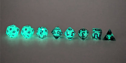 A straight on photo of a complete set of polyhedral dice that have glowing green spherical inserts and have purple numbers arranged in a straight line. They are lined up with the 2 d20s on the left going down to the d4 on the right side. The highest value number of each die is facing up. This image shows the glow-in-the-dark feature of this dice set and that you can still see the black swirls through the glow.