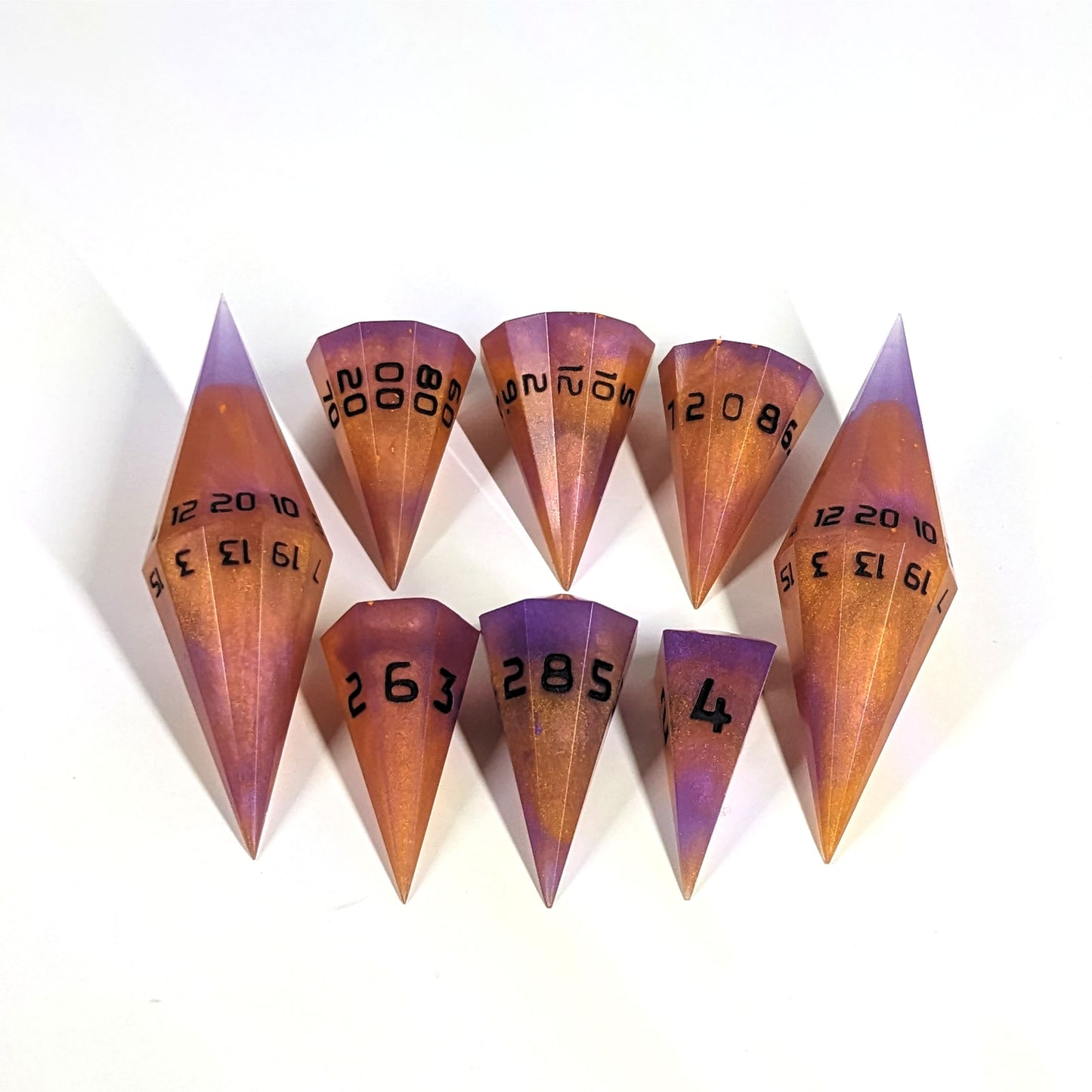 A dagger style DnD dice set that is purple and orange with black numbers is arranged with a d20 each on the right and left, with the d%, d12, and d10 along the top and the d6, d8, and d4 along the bottom, all in line with the d20s.