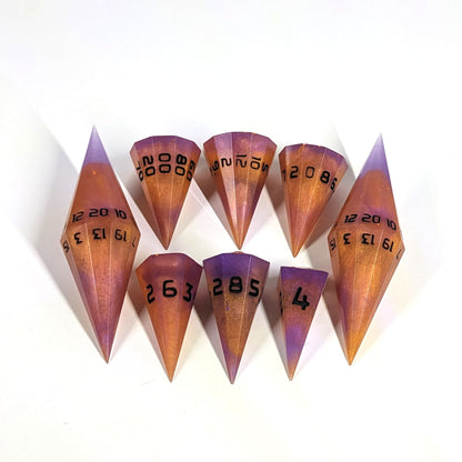 A dagger style DnD dice set that is purple and orange with black numbers is arranged with a d20 each on the right and left, with the d%, d12, and d10 along the top and the d6, d8, and d4 along the bottom, all in line with the d20s.