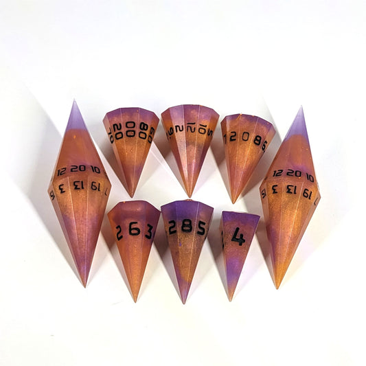 The dagger style DnD dice set that is purple and orange with black numbers is arranged with a d20 each on the right and left, with the d%, d12, and d10 along the top and the d6, d8, and d4 along the bottom, all in line with the d20s.