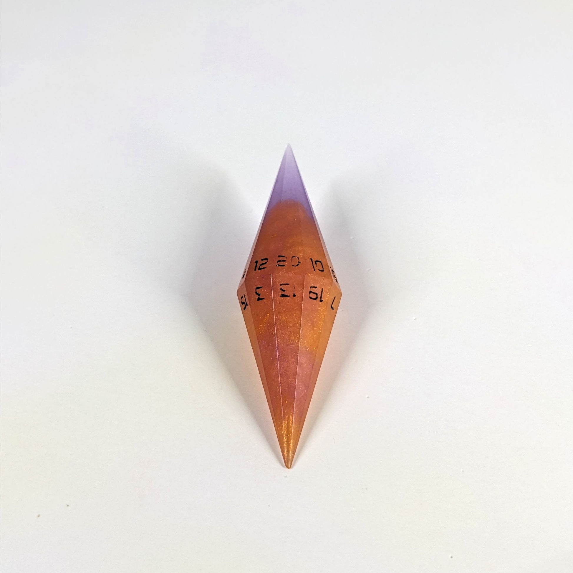 A high angle shot of a purple and orange diamond d20 with black numbers on a white background.