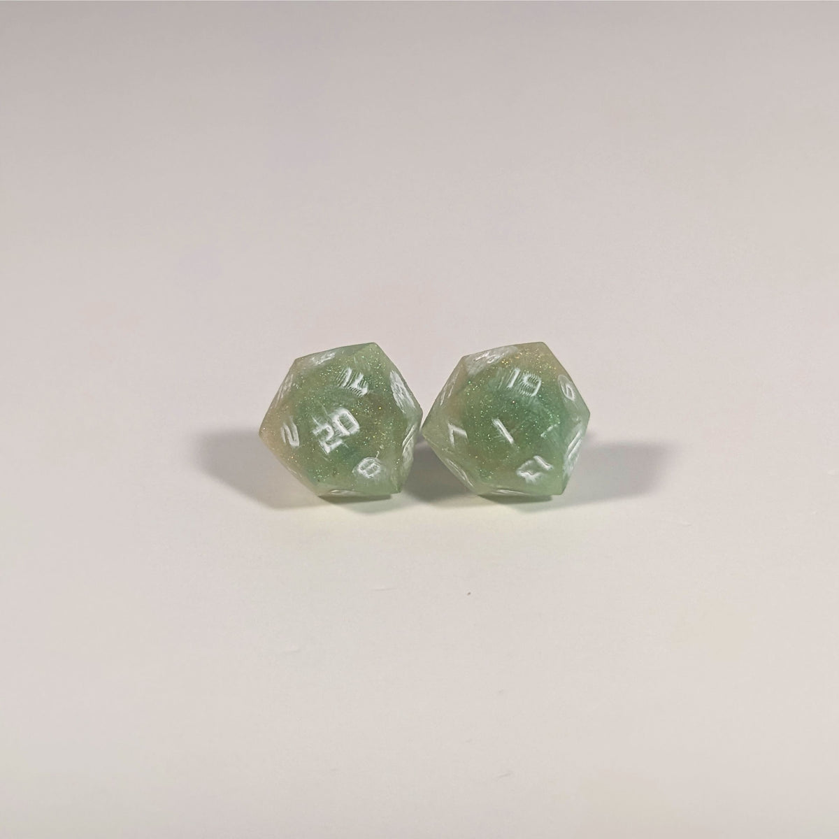 A single pair of the larger size handmade d20 earrings with titanium hardware that are bright green and red gold with white numbers on a white background. The earring on the left centers the 20 face and the earring on the right centers the 1 face.