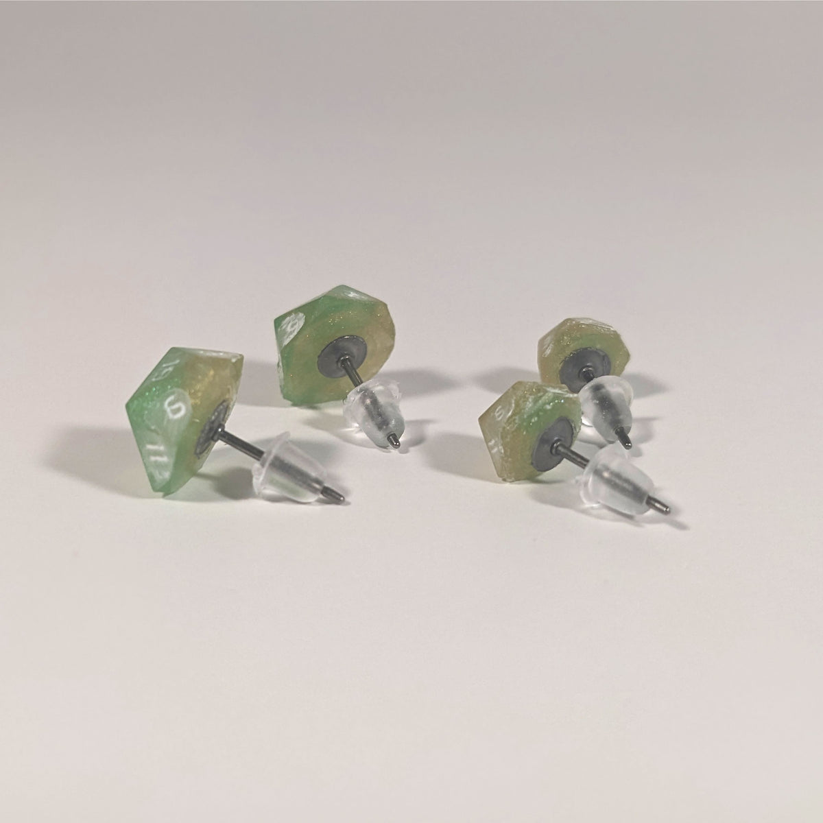 Two pairs of handmade d20 earrings that are bright green and red gold with white numbers turned to show the titanium hardware and bell shaped rubber backs.