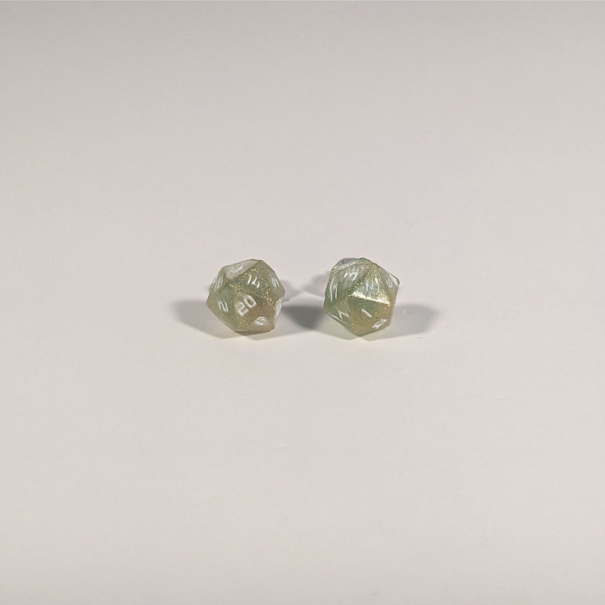 A single pair of the smaller size handmade d20 earrings with titanium hardware that are bright green and red gold with white numbers on a white background. The earring on the left centers the 20 face and the earring on the right centers the 1 face.