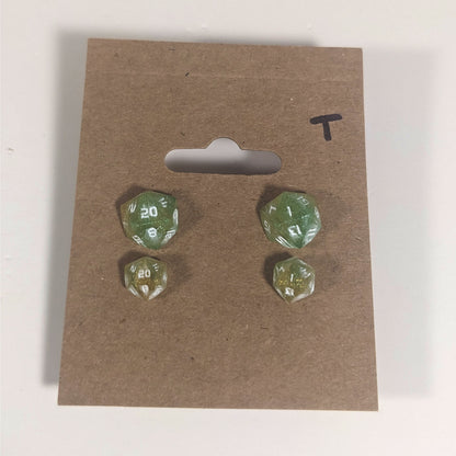 Two pairs of handmade d20 earrings with titanium hardware that are bright green and red gold with white numbers on a kraft brown earring card with a T in the top right corner. The earrings on the left of each pair centers the 20 face and the earrings on the right of each pair centers the 1 face.