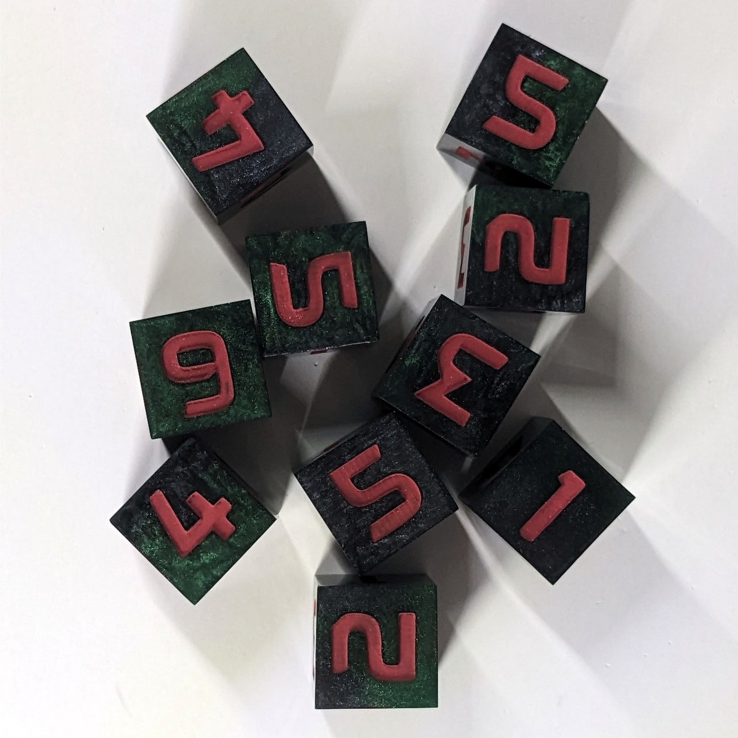 A top down view of ten standard six sided dice sit on a white background. The dice are black and dark green with red numbers.