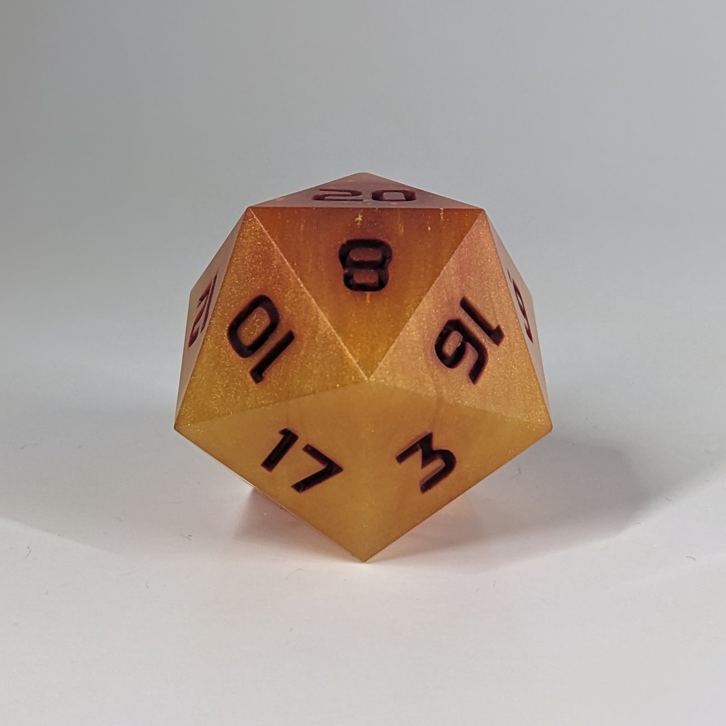 A straight on photo of a large d20 that has swirls of orange, yellow, and a small amount of red with dark red numbers on a white background.