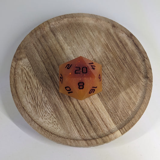 A high angle view of a large d20 with swirls of orange, yellow, and a small amount of red with dark red numbers. It is sitting in the center of a wooden circle.