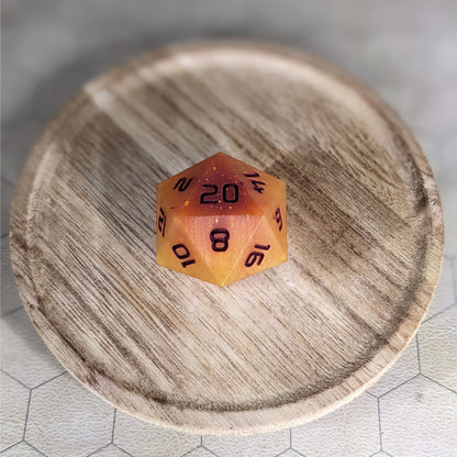 A high angle view of a large d20 with swirls of orange, yellow, and a small amount of red with dark red numbers. It is sitting in the center of a wooden circle.