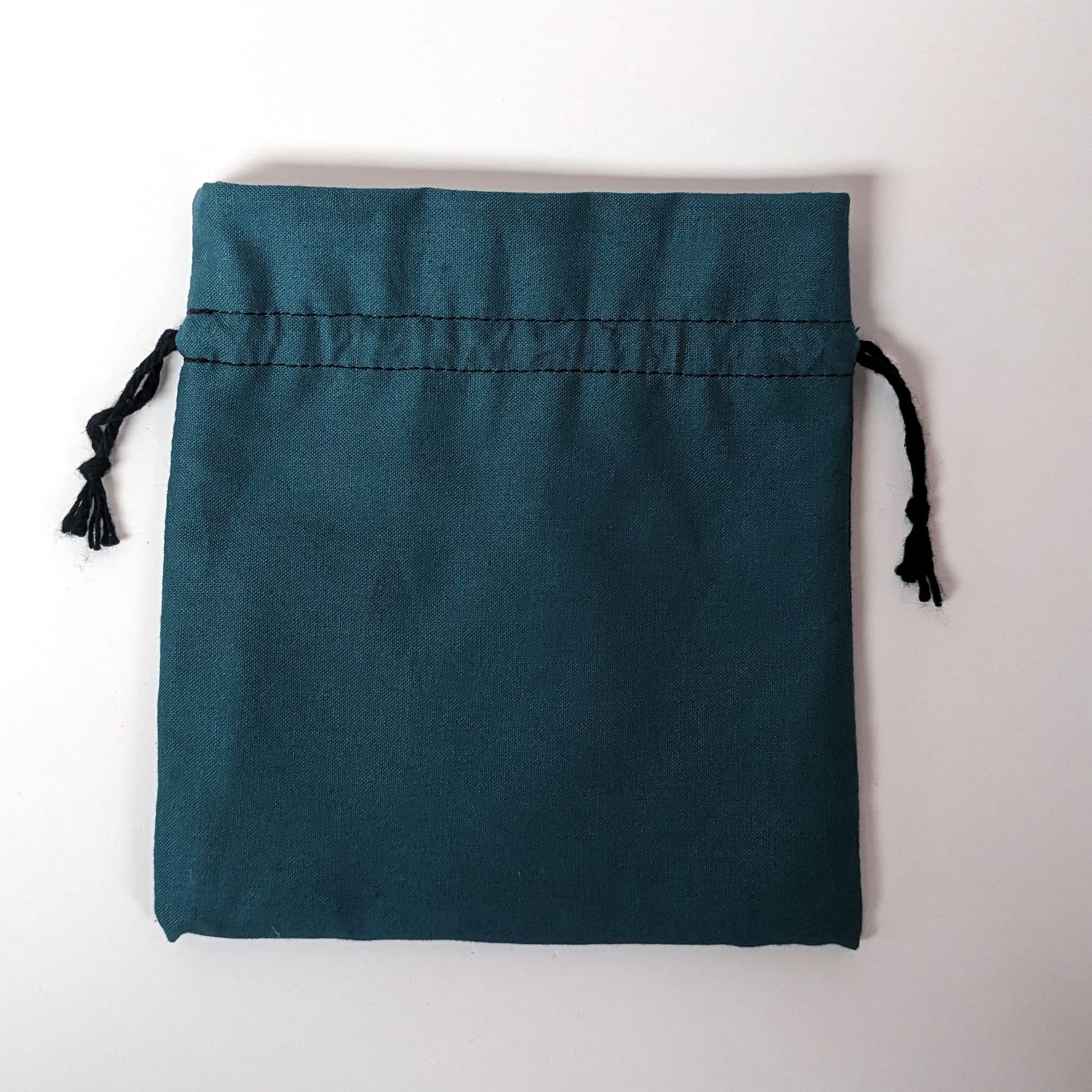 A teal, medium size dice bag lies flat and black drawstrings untightened on a white background.