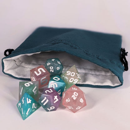 Colorful polyhedral d&d dice spill out of the open mouth of a teal, medium size dice bag. It shows the interior of the bag, which is a white flannel fabric, and the drawstrings are black.
