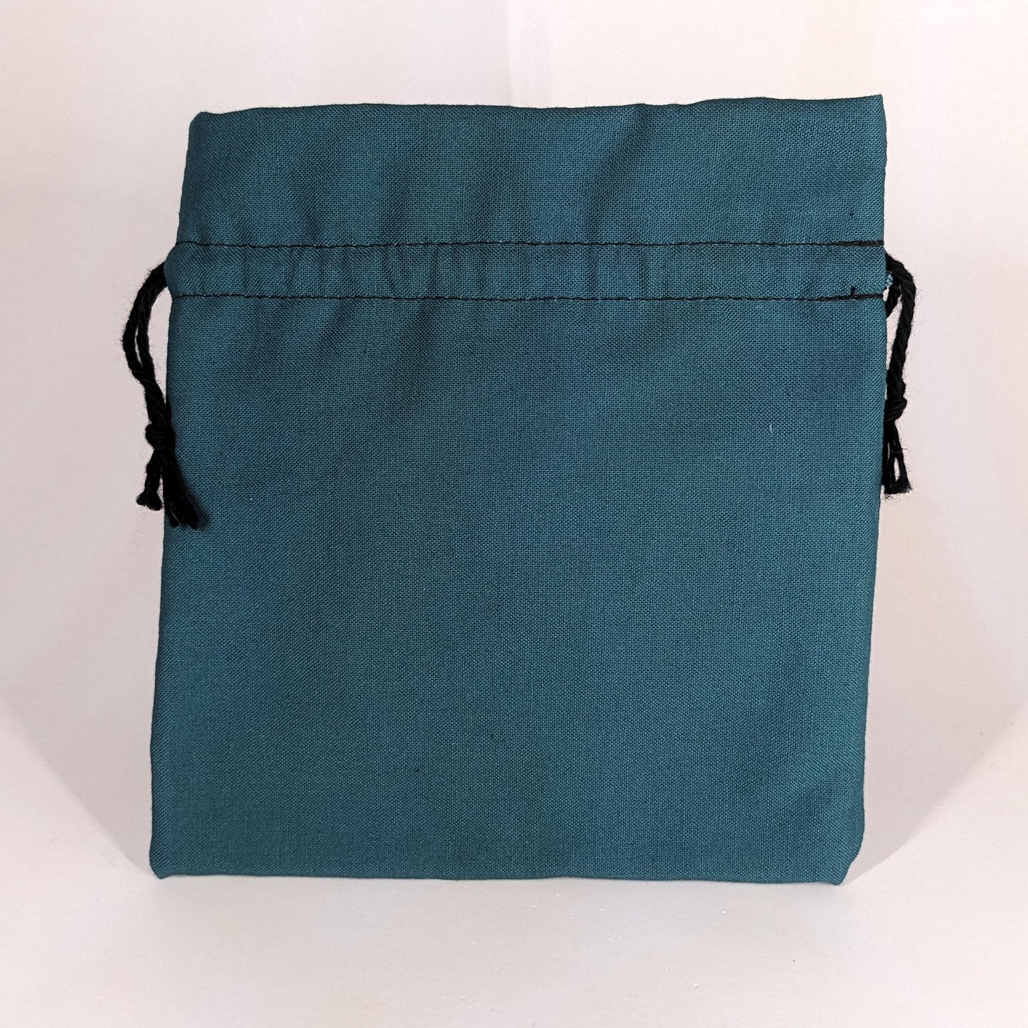 A teal, medium size dice bag that is sitting upright and not tied closed. The black drawstrings are visible on each side of the bag.