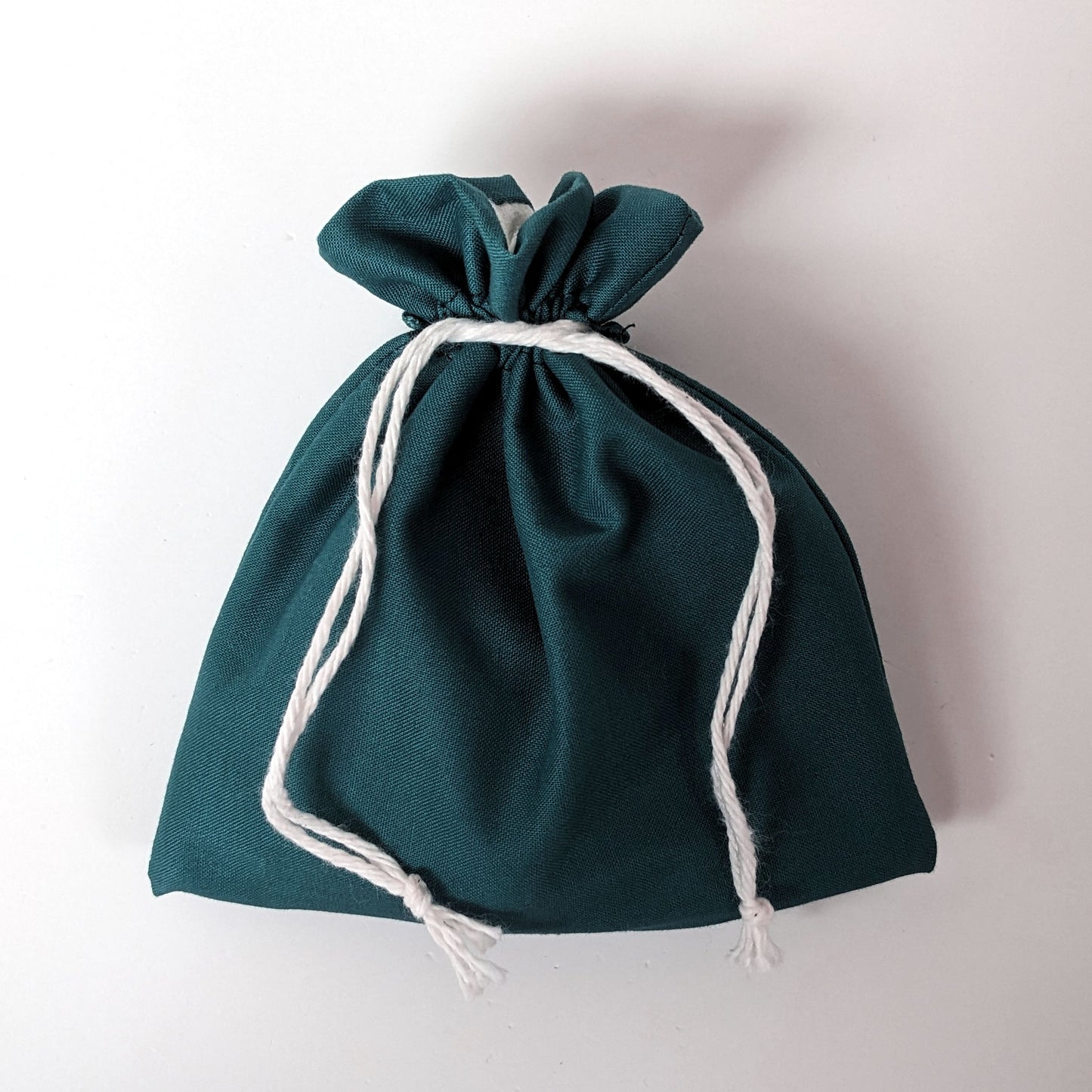 A handmade, teal, medium size dice bag is tied closed by it's black drawstrings.