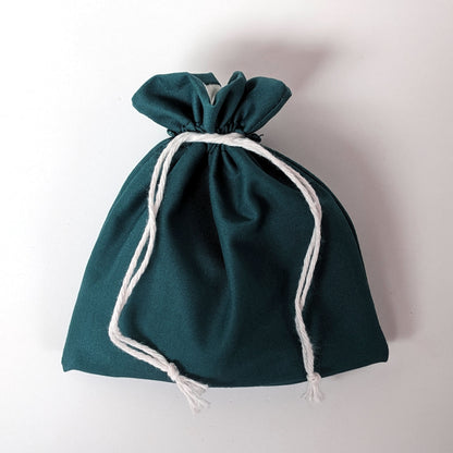 A handmade, teal, medium size dice bag is tied closed by it's black drawstrings.