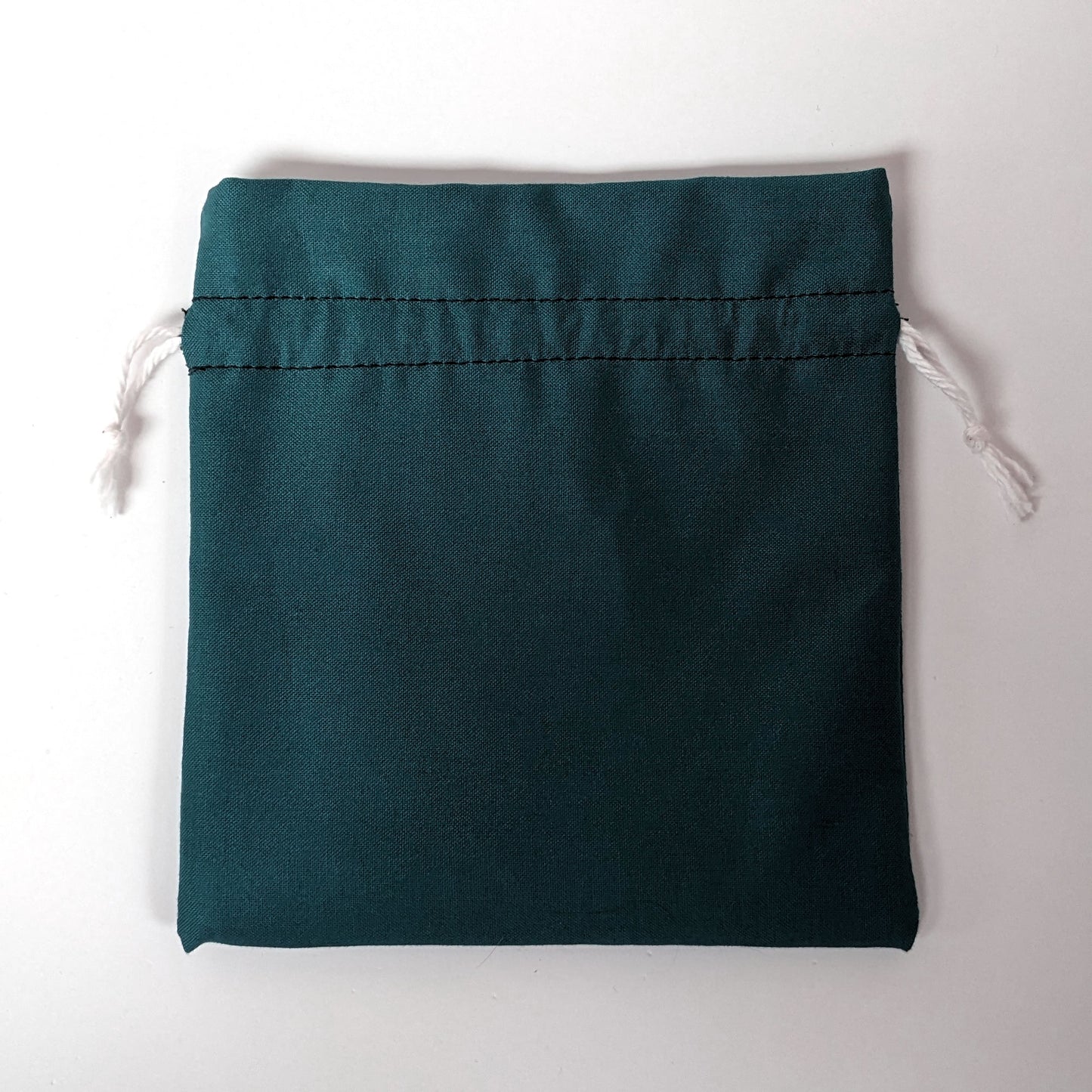 A teal, medium size dice bag lies flat and white drawstrings untightened on a white background.