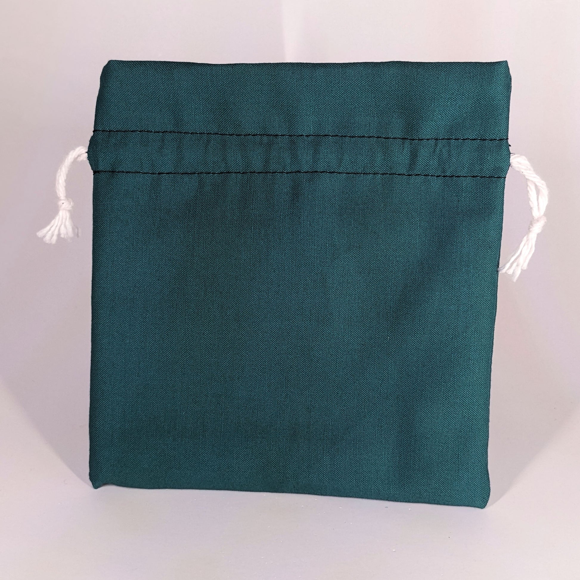 A teal, medium size dice bag that is sitting upright and not tied closed. The white drawstrings are visible on each side of the bag.