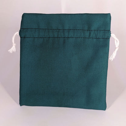 A teal, medium size dice bag that is sitting upright and not tied closed. The white drawstrings are visible on each side of the bag.