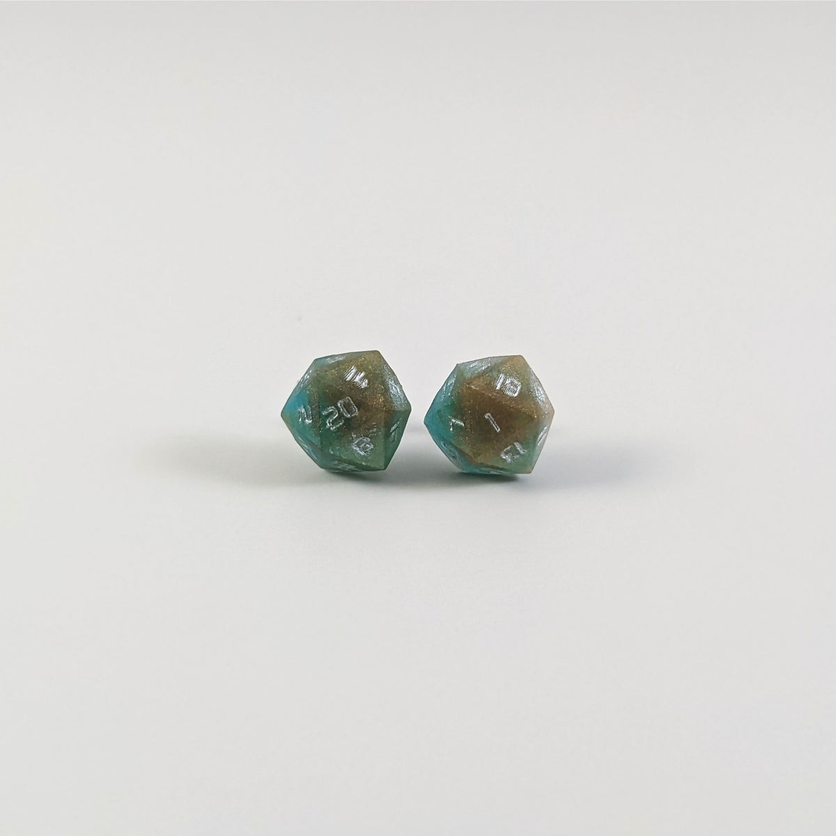 A single pair of the larger size handmade d20 earrings with titanium hardware that are teal and copper swirls with silver numbers on a white background. The earring on the left centers the 20 face and the earring on the right centers the 1 face.